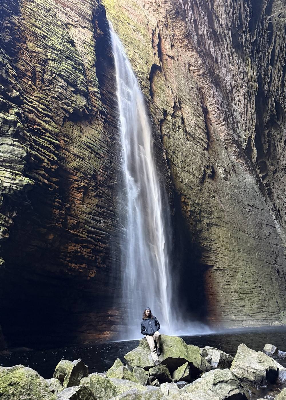 Michele pequena diante de uma cachoeira alta