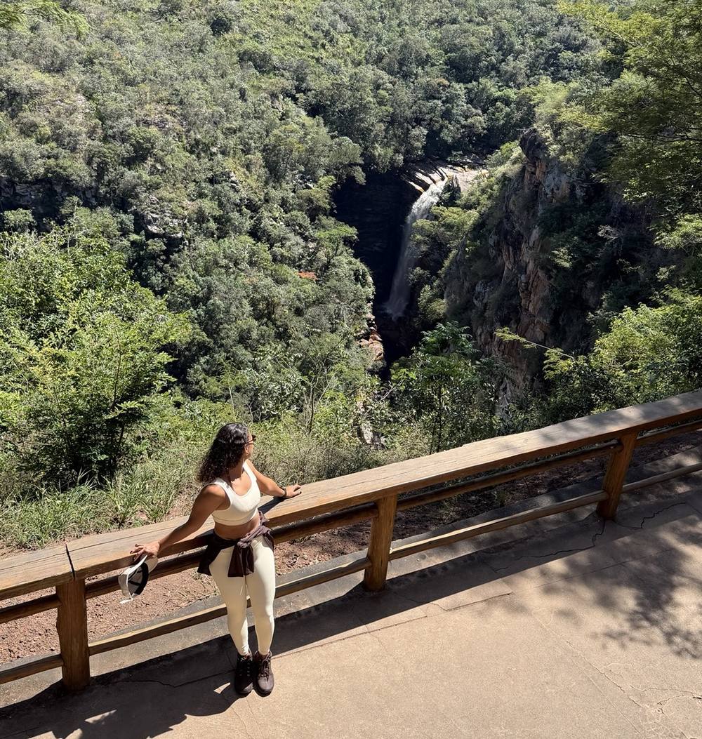 Michele em um mirante de madeira diante de uma cachoeira na mata