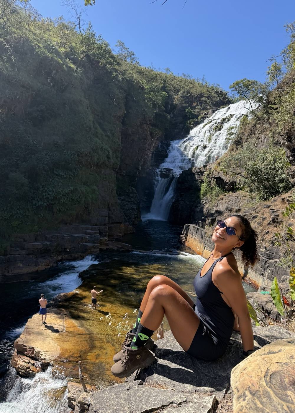 Michele sentada na rocha ao lado de uma queda d'água